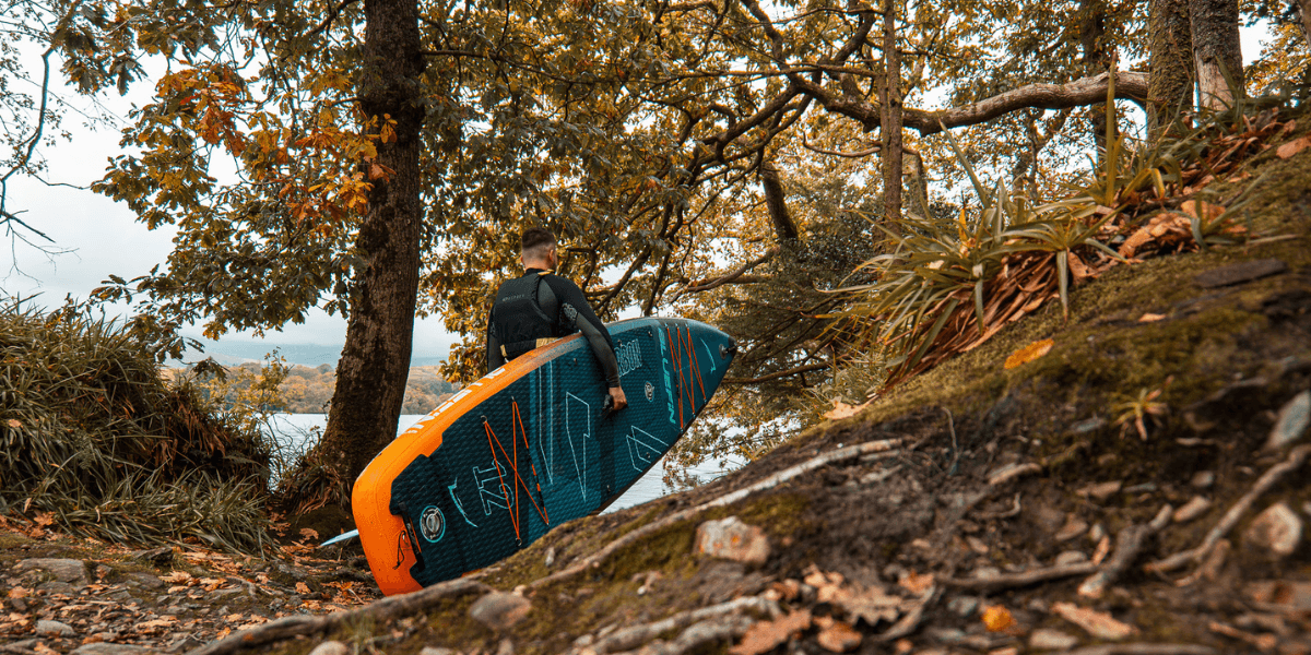 Man holding onto a paddleboard in an autumn forrest