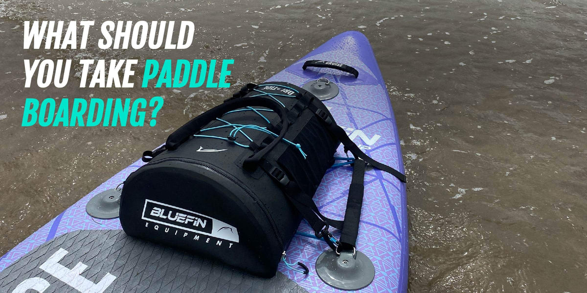 Purple paddleboard carrying a black equipment bag on shallow water, with text asking what to take paddleboarding