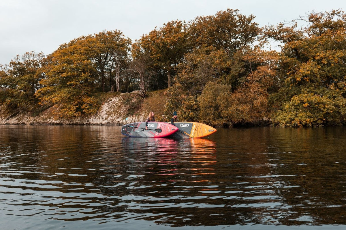 two women stood in a lake with their paddleboards during autumn
