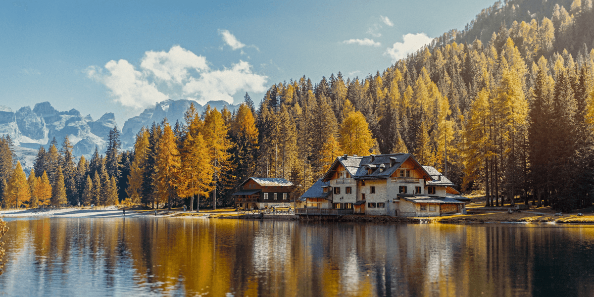 Alpensee, der einen Herbstwald und ein Chalet spiegelt, mit zerklüfteten Bergen im Hintergrund