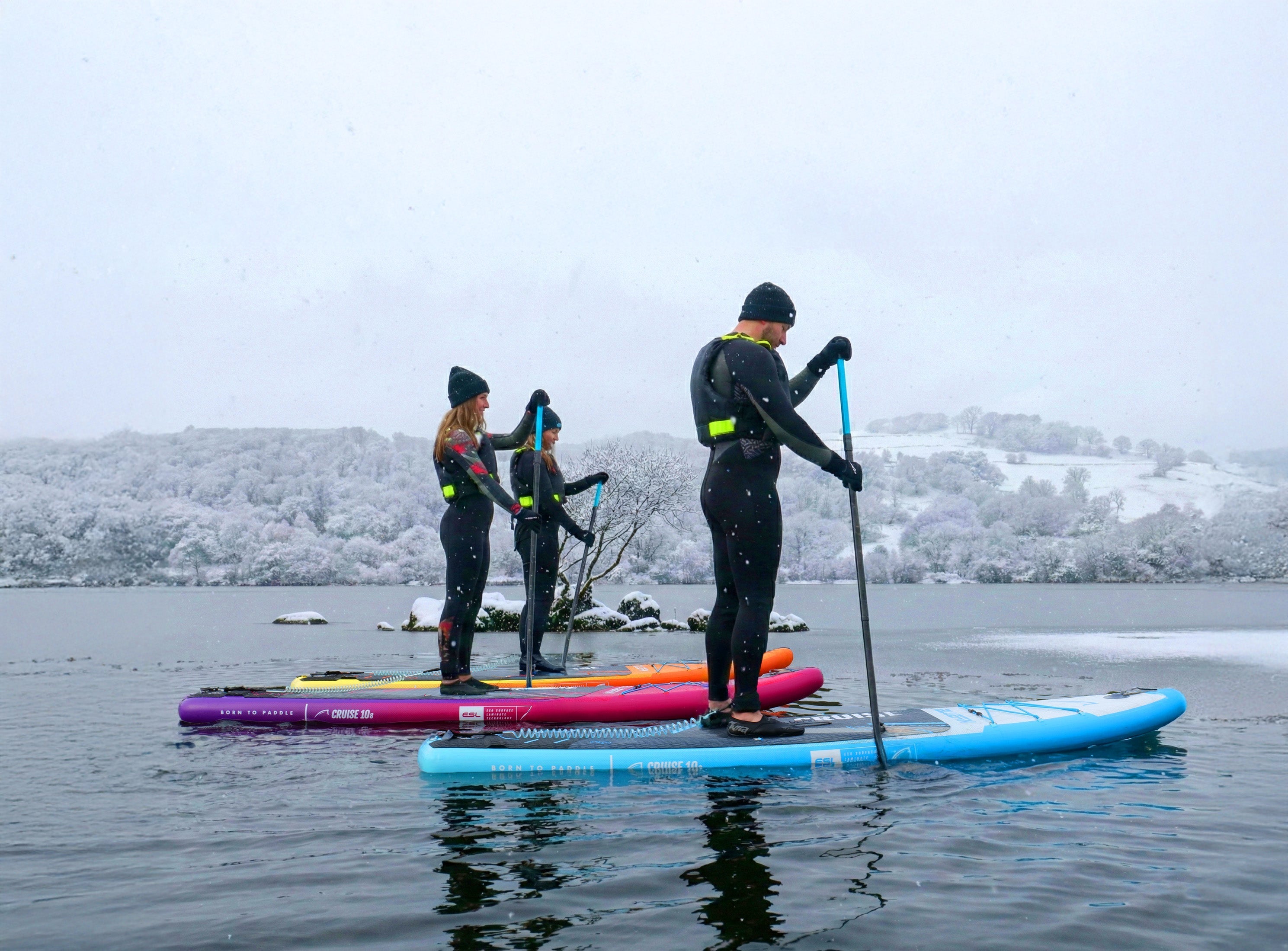 three people paddleboarding in snowy conditions