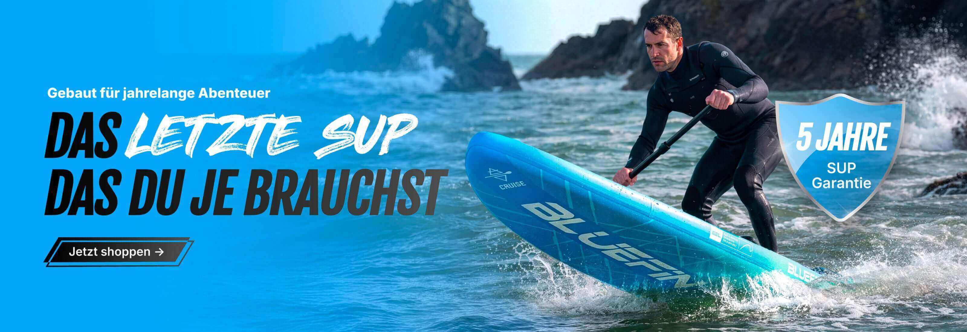 Man paddling a blue inflatable SUP on water, wearing a wetsuit, with rocky shore in background