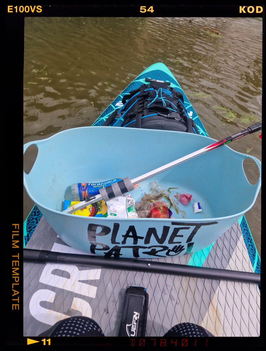 Paddleboard with a blue container filled with trash, including bottles and wrappers, on a water surface.
