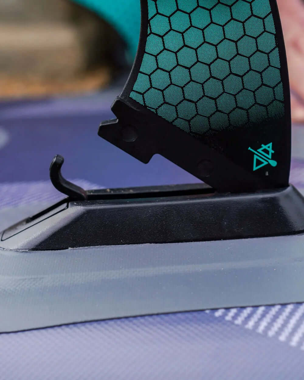 Close-up of a paddleboard fin attachment with a hexagonal pattern and black base on a textured surface