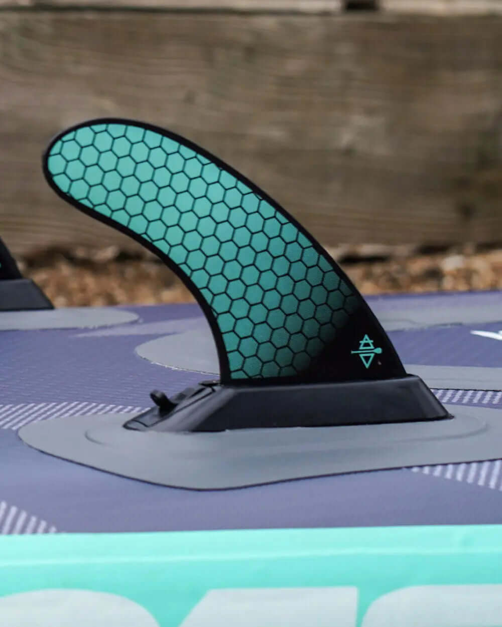 Close-up of a paddleboard fin with a honeycomb pattern, mounted on a textured surface.