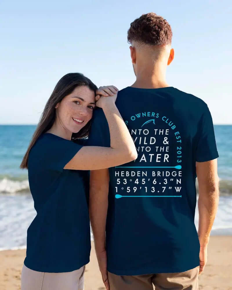 Couple wearing matching navy t-shirts with text on beach, woman smiling and touching man's shoulder