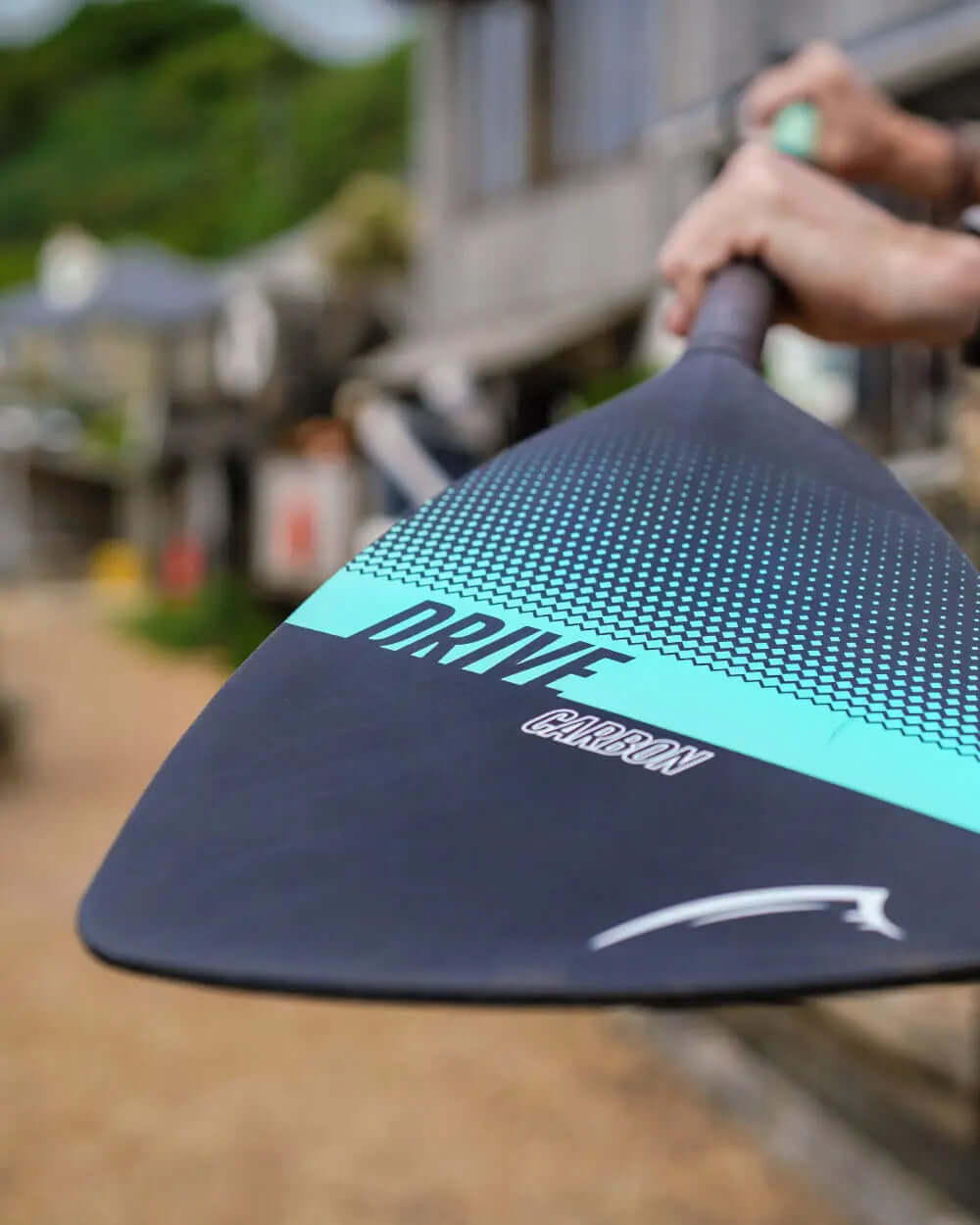 Close-up of a carbon paddle blade with turquoise and black design, featuring the word 'DRIVE
