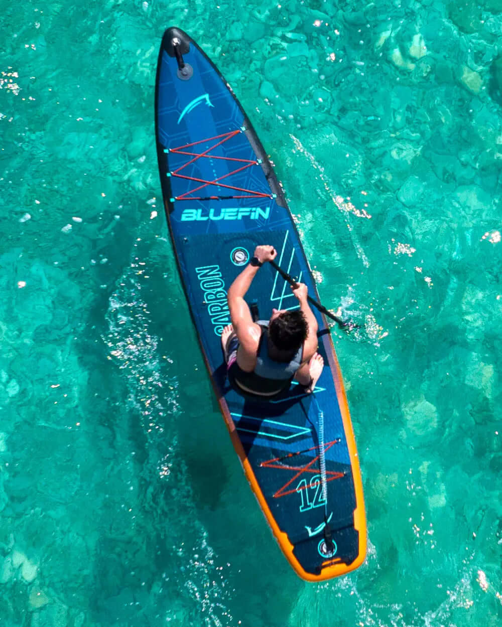 Person paddling a Bluefin inflatable paddleboard on clear turquoise water