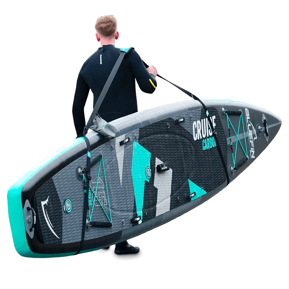 Person in wetsuit carrying a Bluefin Cruise Carbon paddleboard with a textured surface and center fin