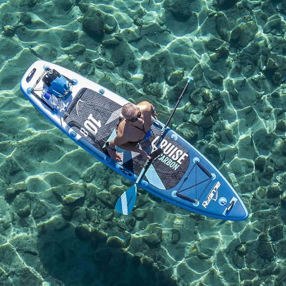 Person, die ein blaues aufblasbares Paddleboard über klares Wasser mit sichtbaren Steinen darunter paddelt