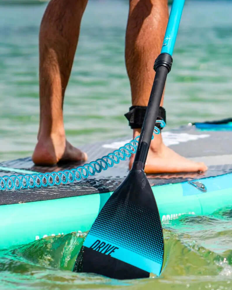 Person on a paddleboard using a black paddle with blue accents, water splashing around the paddle