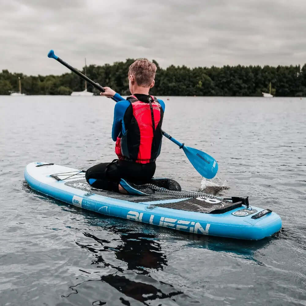 Person paddling on a blue inflatable paddleboard with a textured deck pad on calm water