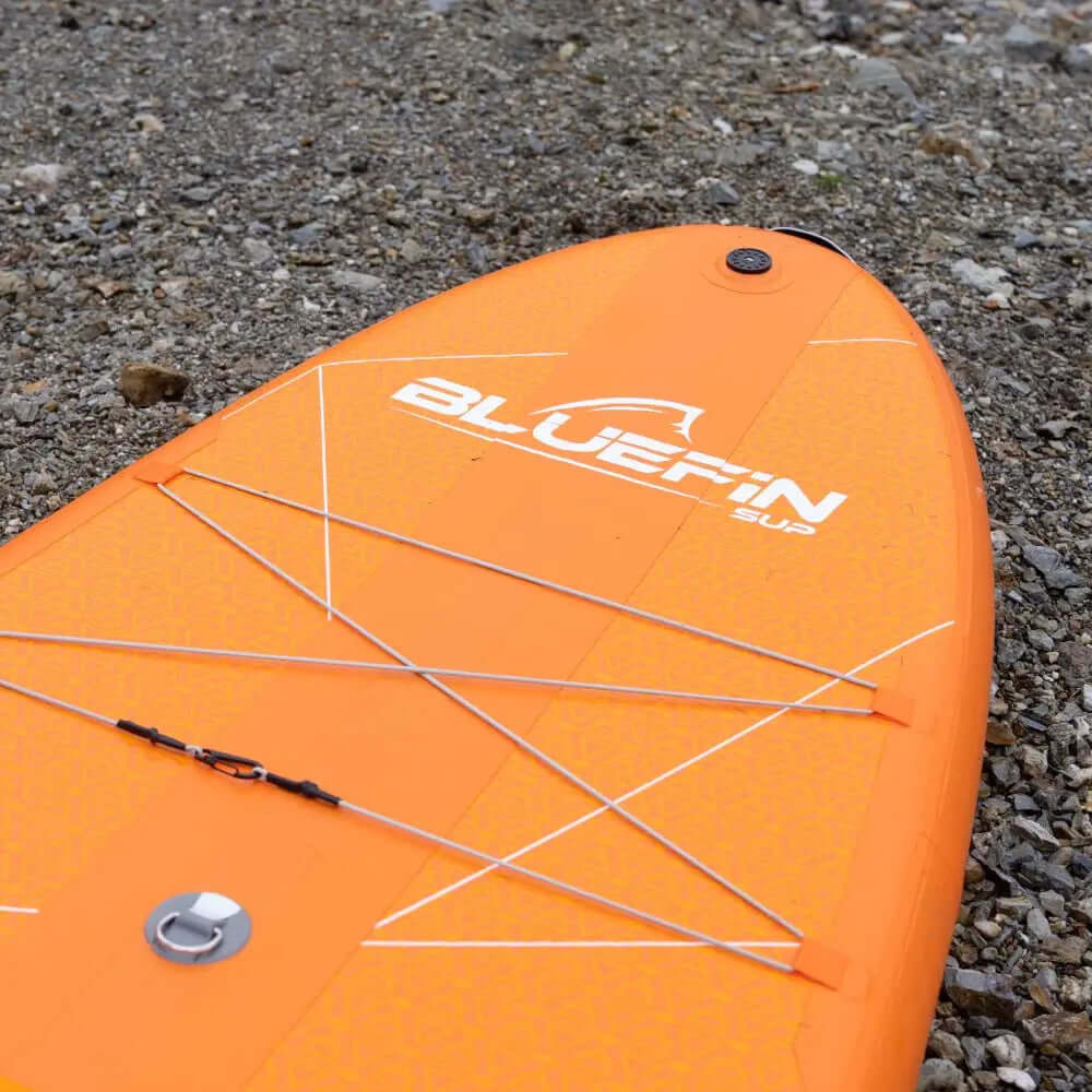 Inflatable paddleboard in bright orange with textured surface and bungee cord storage on top