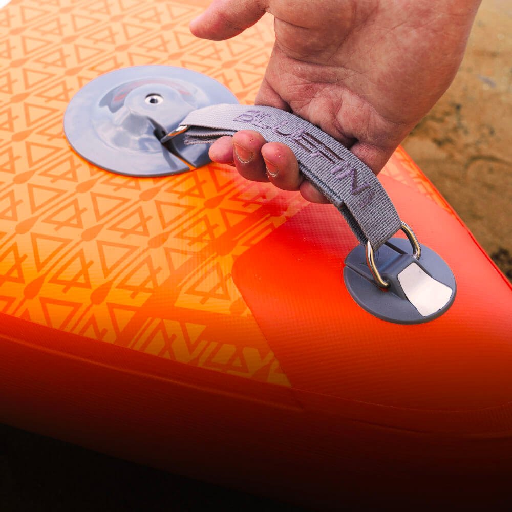 Hand holding gray strap on orange inflatable paddleboard with textured surface and valve