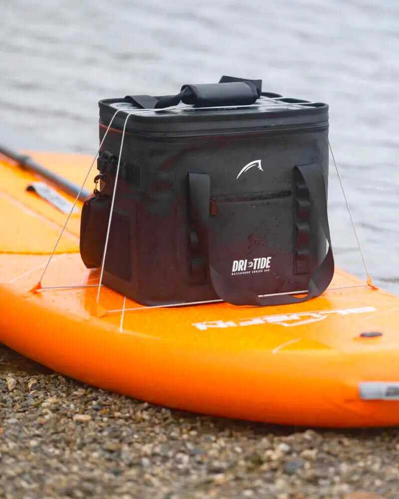 Black waterproof cooler bag on an orange paddleboard by the water's edge