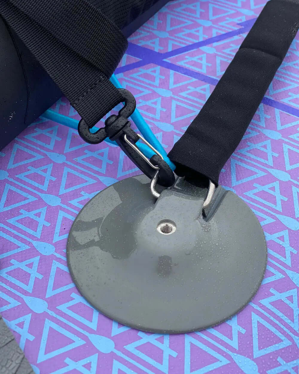 Close-up of a gray fin attachment on a paddleboard with black straps and a colorful deck pad.