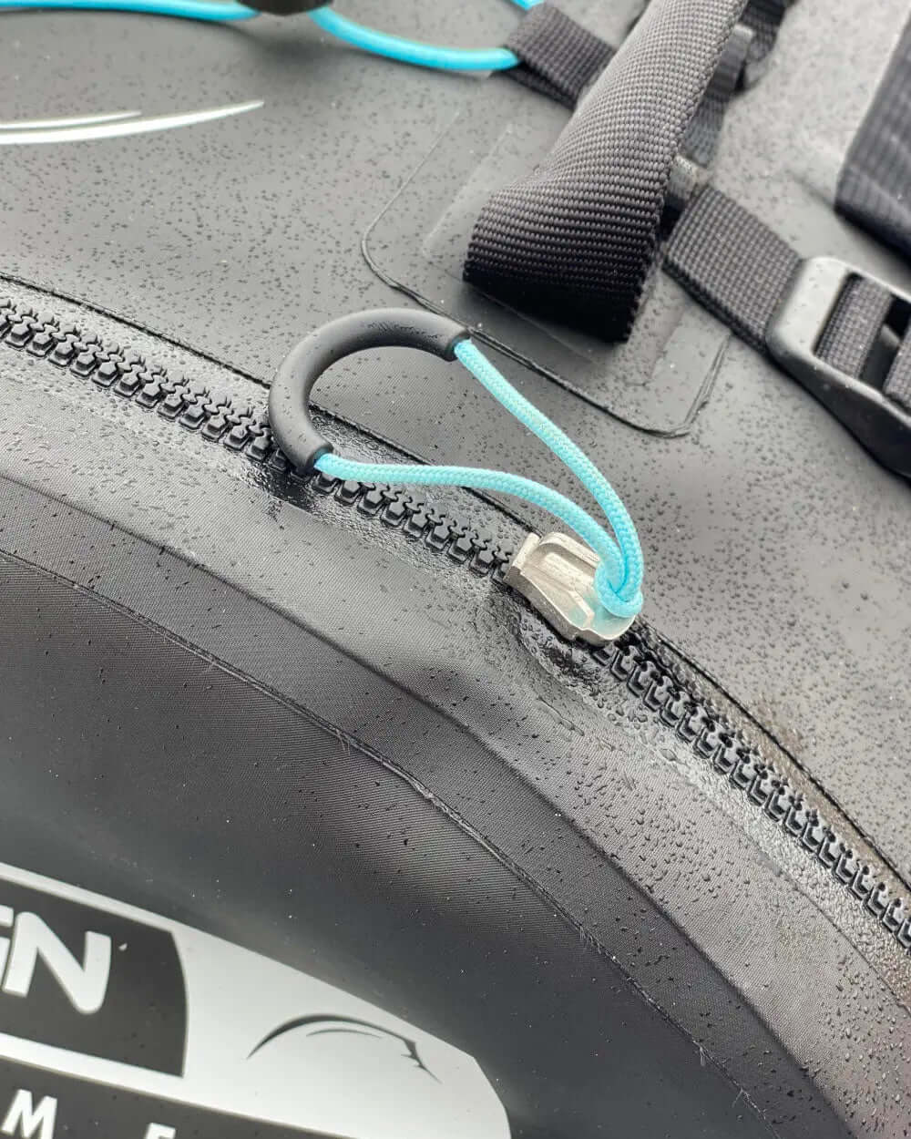 Close-up of a waterproof zipper with a blue pull cord on a black surface, showing droplets of water.