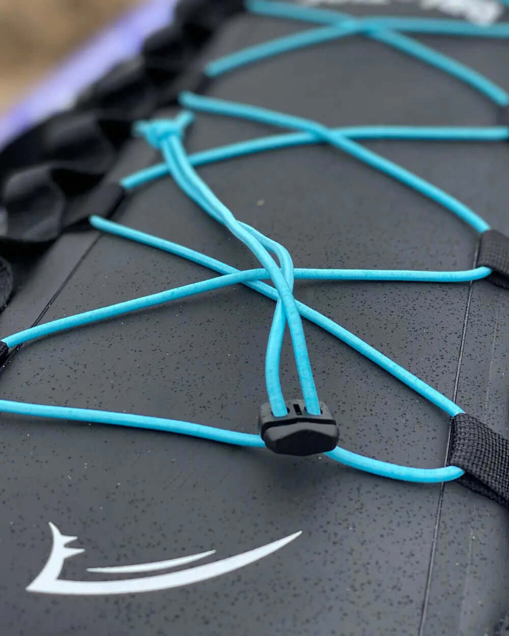 Close-up of black paddleboard deck with blue bungee cords and a white logo