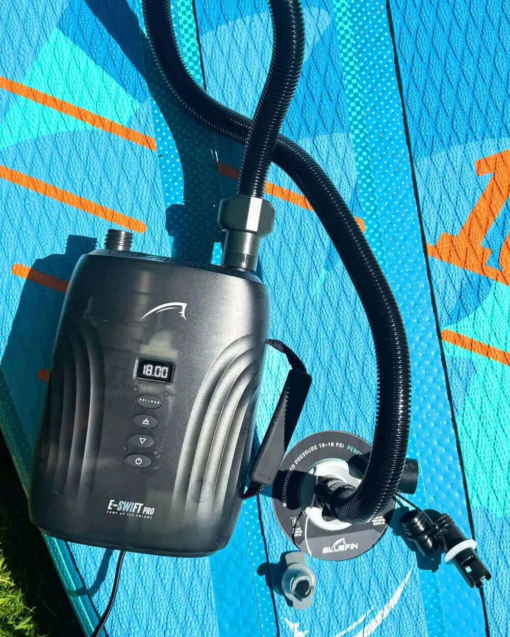 Electric pump on a blue paddleboard, with a hose connected to the inflation valve.