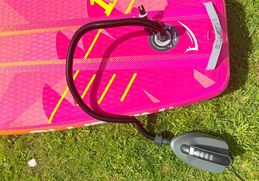 Inflatable paddleboard in pink with a black inflation hose and valve on a grassy surface