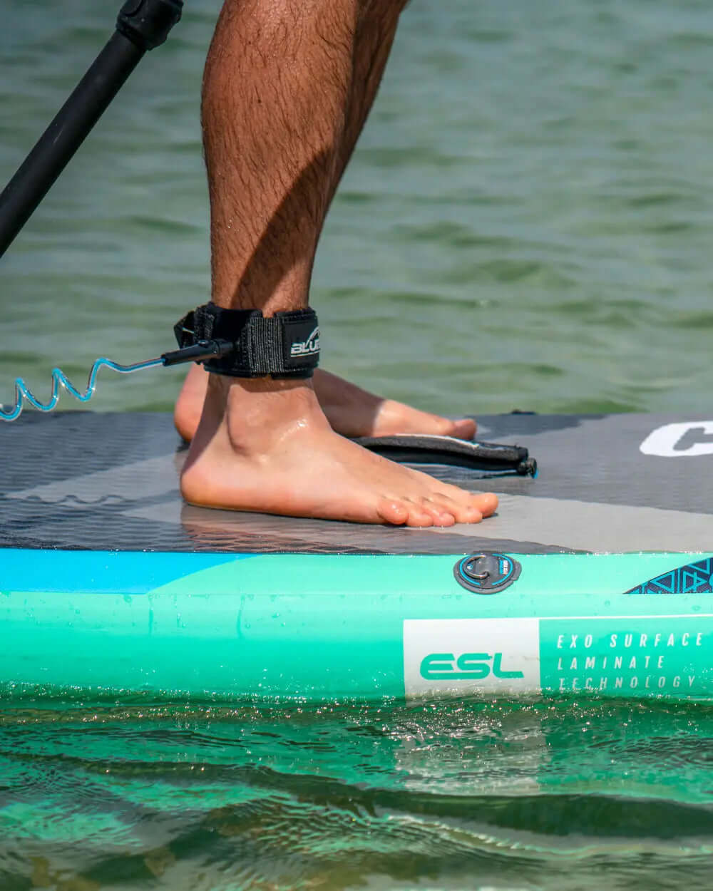Close-up of bare feet on a paddleboard with ankle leash, water visible below