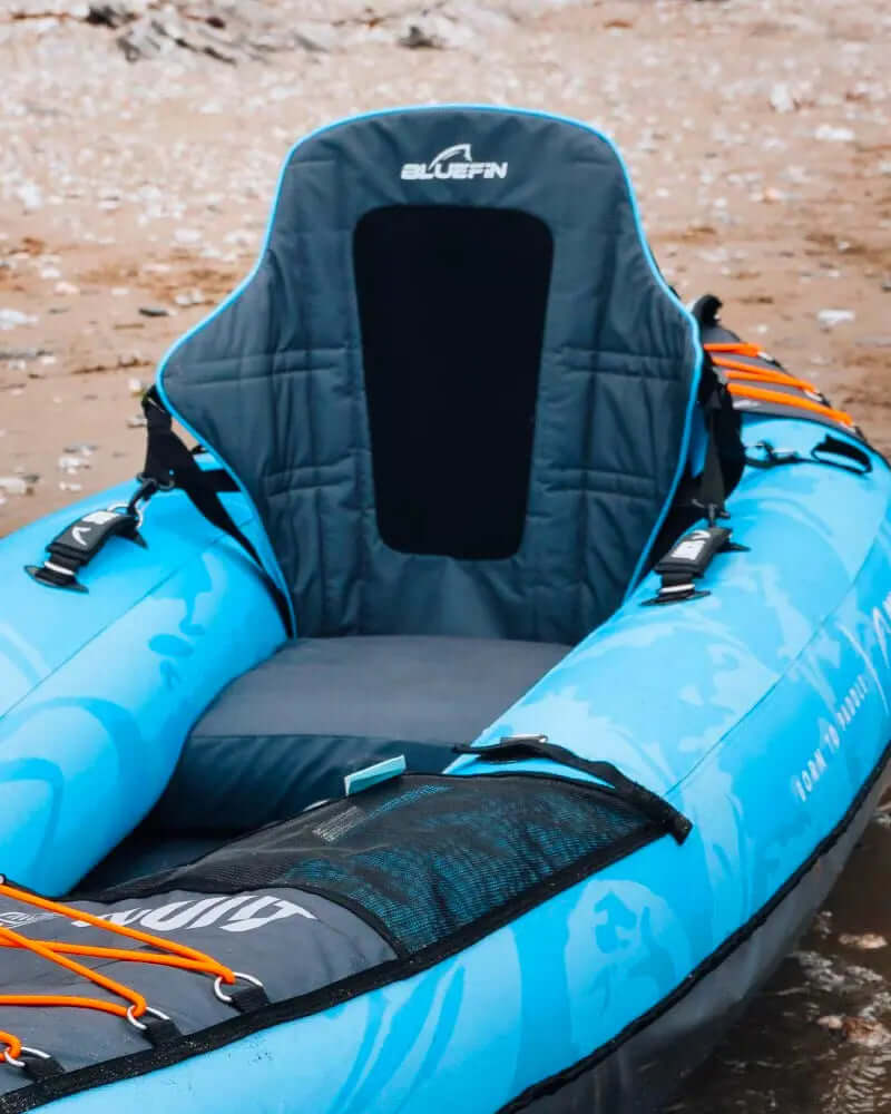 Blue inflatable kayak with a padded seat, adjustable straps, and a textured surface on the bottom.
