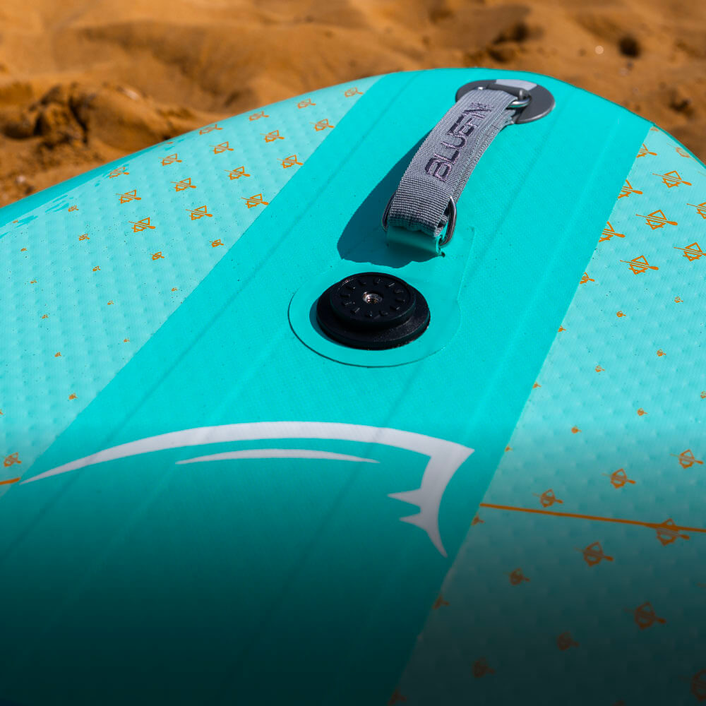 Inflatable paddleboard in turquoise with textured deck, center fin, and inflation valve on sandy beach
