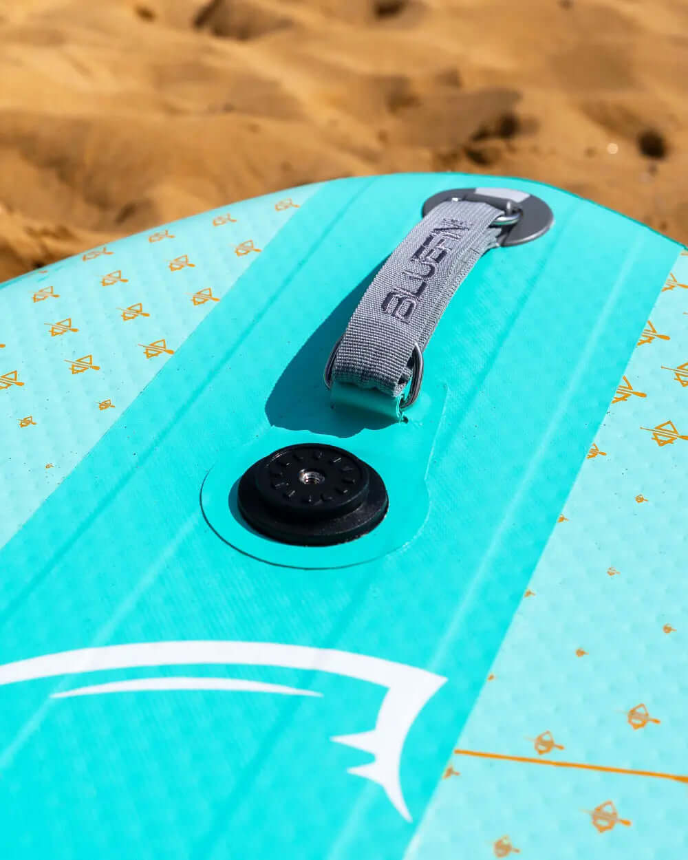 Inflatable paddleboard featuring a textured deck pad, center fin, and inflation valve on a sandy beach