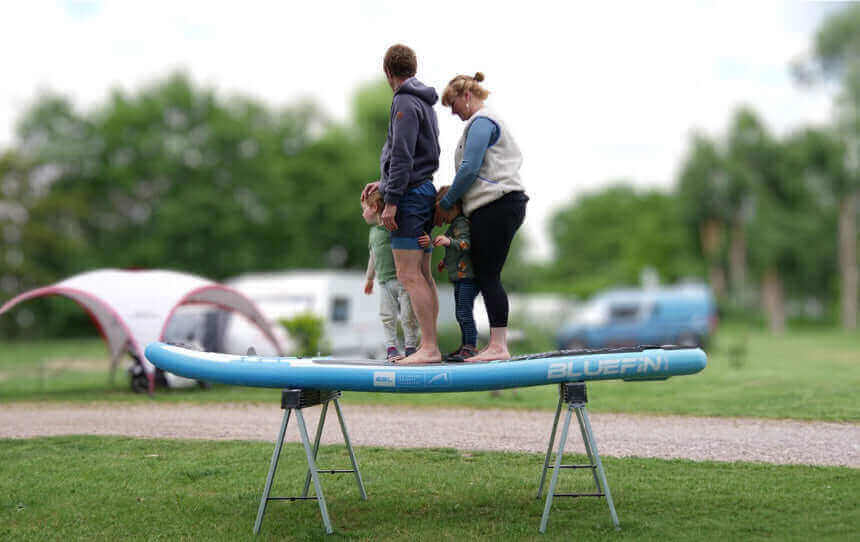Family standing on a Bluefin paddleboard on a support frame in a grassy area.