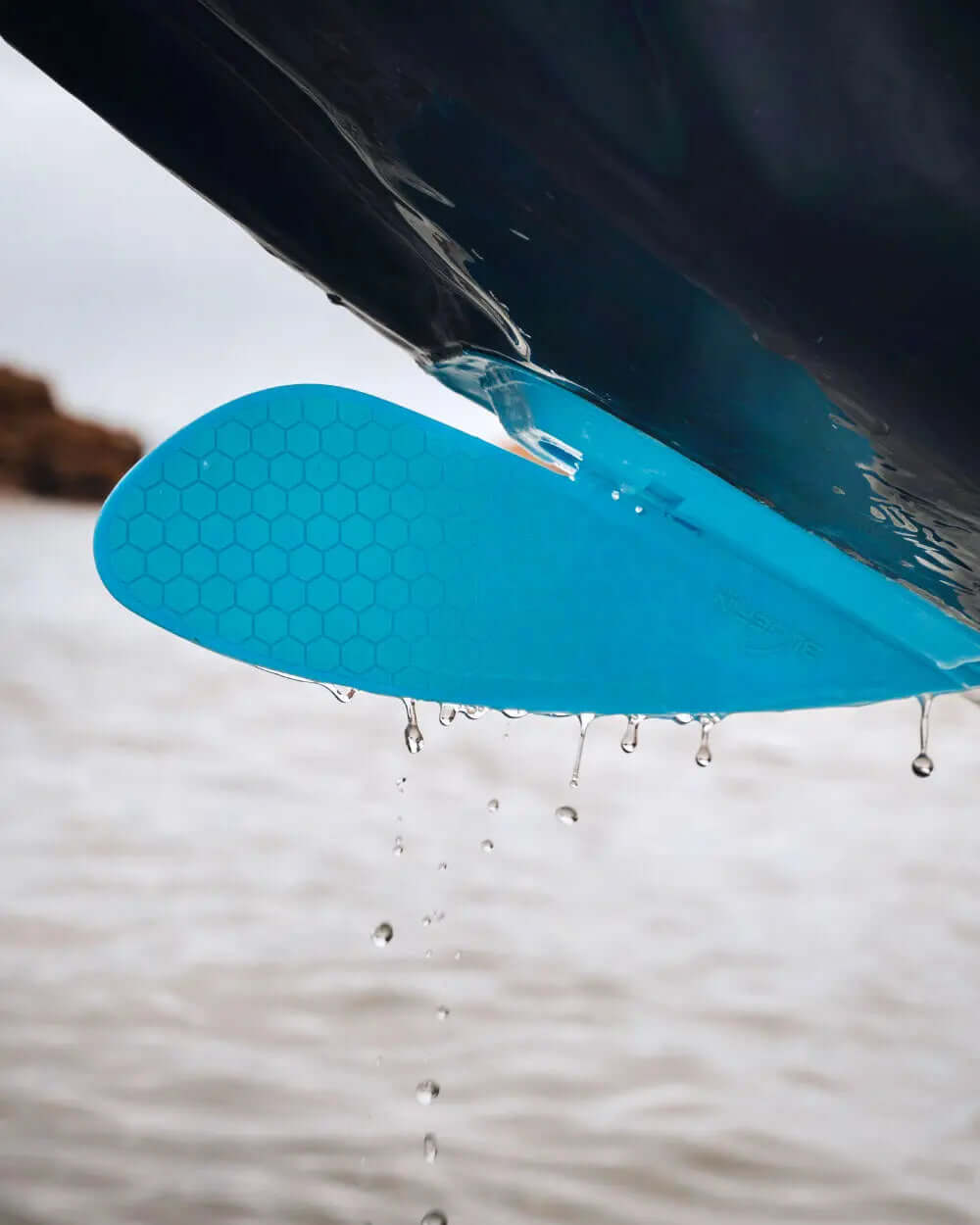 Close-up of a blue honeycomb-patterned fin on a paddleboard, water dripping off it.