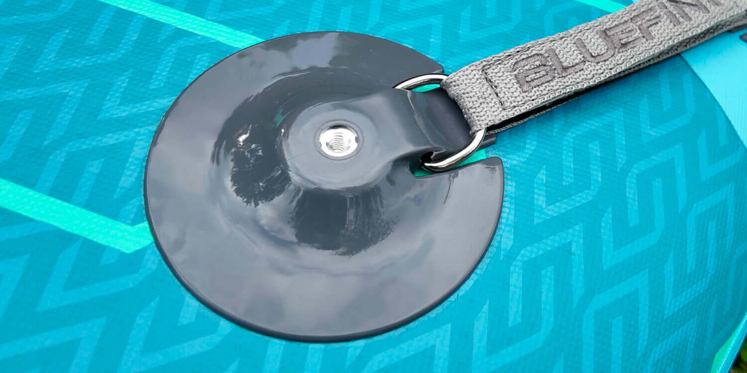 Close-up of a paddleboard's black fin attachment and gray strap on a textured blue surface