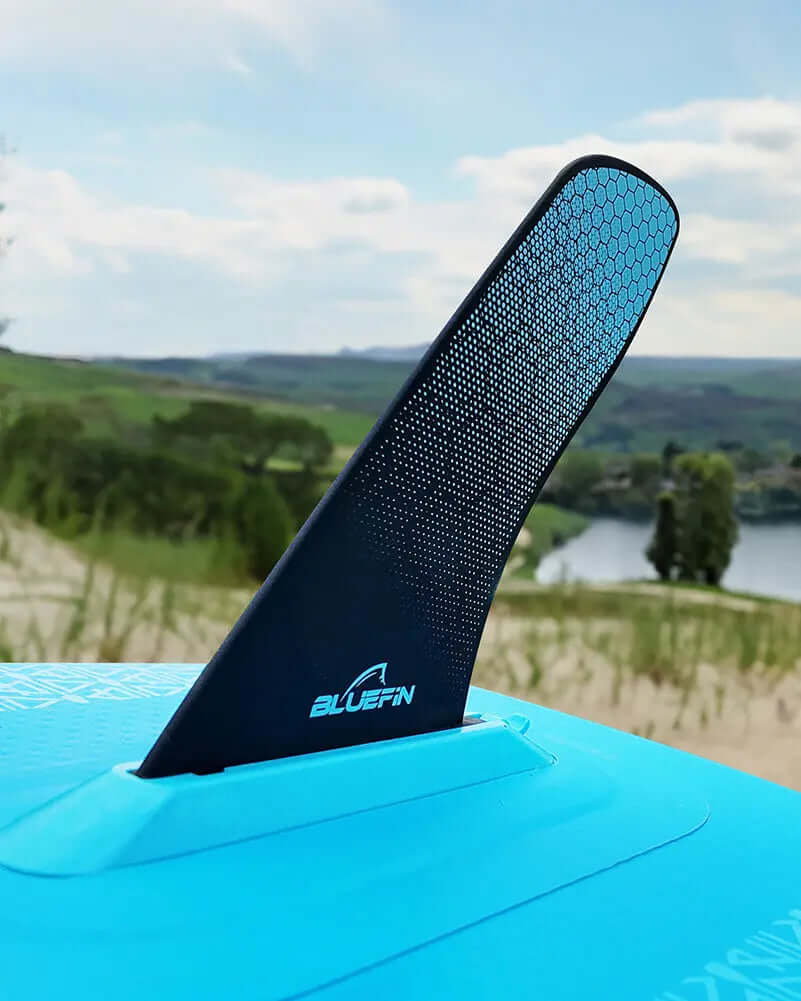 Bluefin paddleboard fin in black with a textured surface, mounted on a blue board against a scenic background.