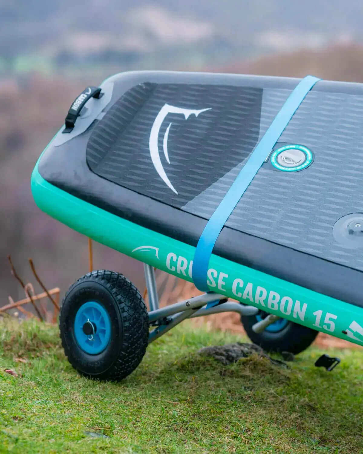 Inflatable paddleboard with a textured deck, blue strap, and wheel for easy transport on grass