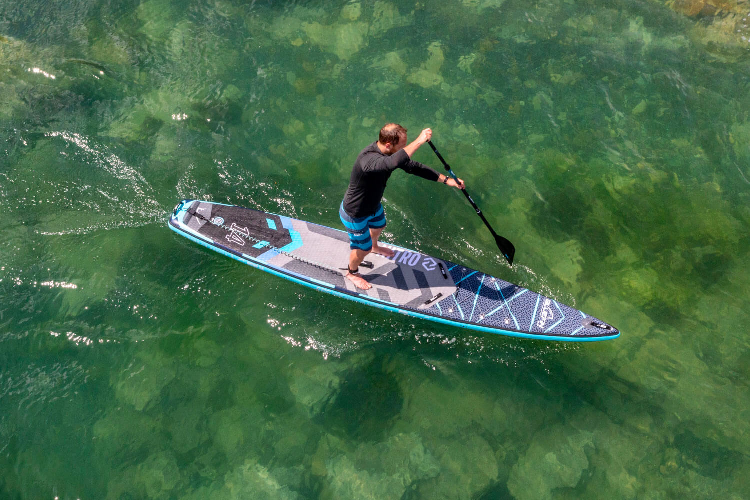 Paddleboarder in black shirt and blue shorts paddling on a blue and gray inflatable paddleboard