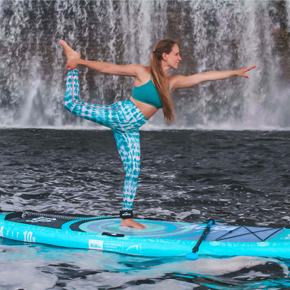 Woman performing yoga on a blue inflatable paddleboard in front of a waterfall.