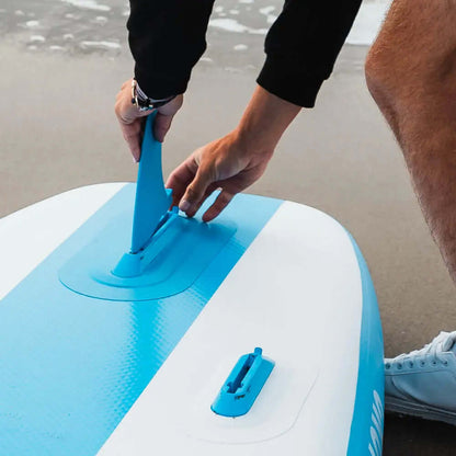 Person attaching a blue fin to an inflatable paddleboard on the beach
