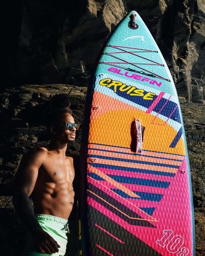 Colorful inflatable paddleboard with textured surface, center fin, and a man in sunglasses beside it
