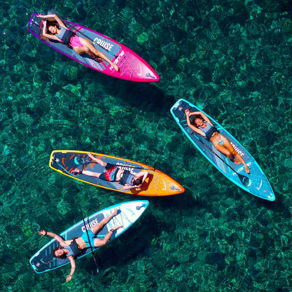 Four paddleboarders relaxing on colorful inflatable paddleboards in clear water.