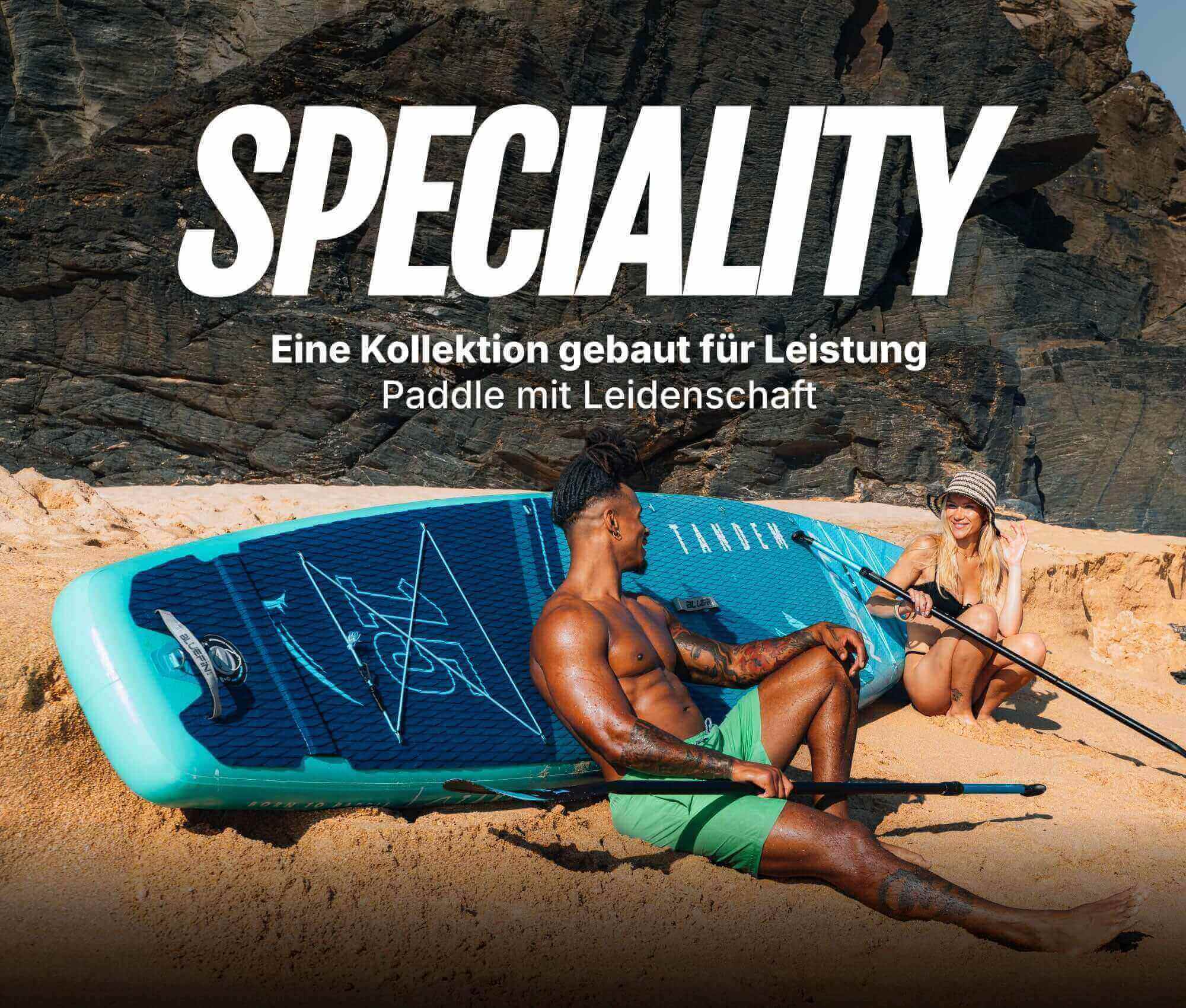 Two people on a beach with an inflatable paddleboard, one sitting and one kneeling, both holding paddles.