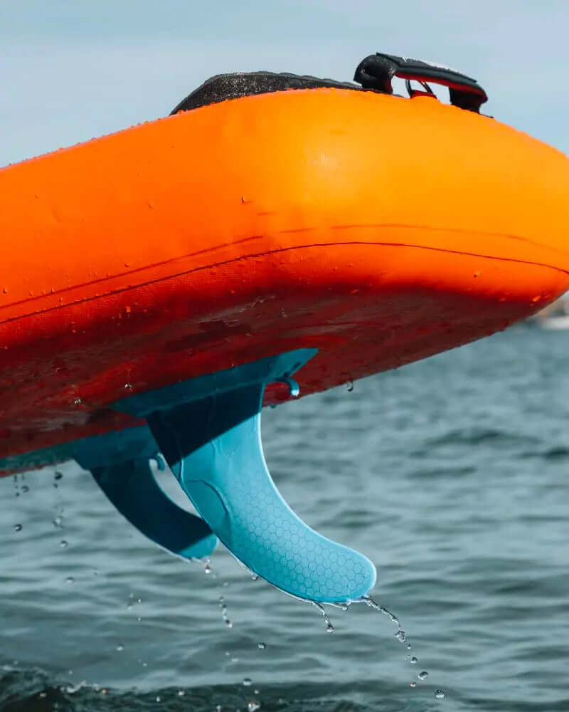 Orange inflatable paddleboard with blue fin partially submerged in water, droplets splashing around