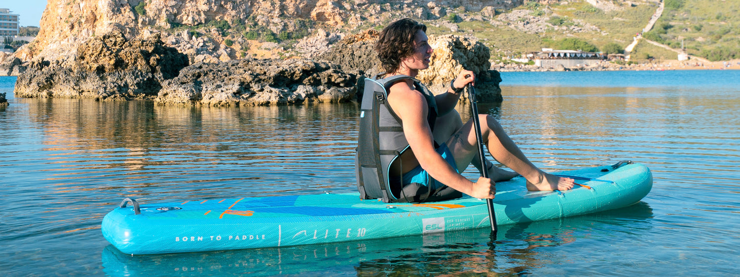 Inflatable paddleboard with textured surface, paddler using a paddle, rocky shore in background