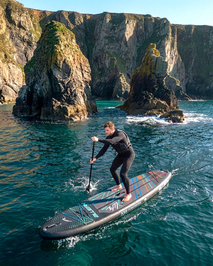 Person paddling on a Bluefin inflatable paddleboard near rocky cliffs in clear water