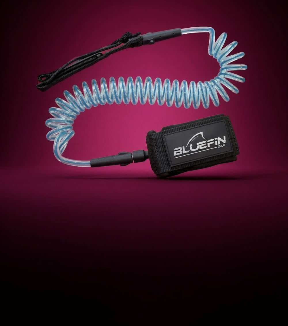 Coiled SUP leash with black neoprene cuff and blue elastic cord on a pink background