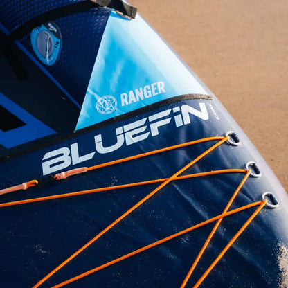 Inflatable paddleboard with blue and navy design, featuring the name Bluefin and orange bungee cords.