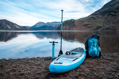 Aufblasbares Paddleboard in Blau mit strukturiertem Deckpad, Pumpe, Paddel und Rucksack am See.