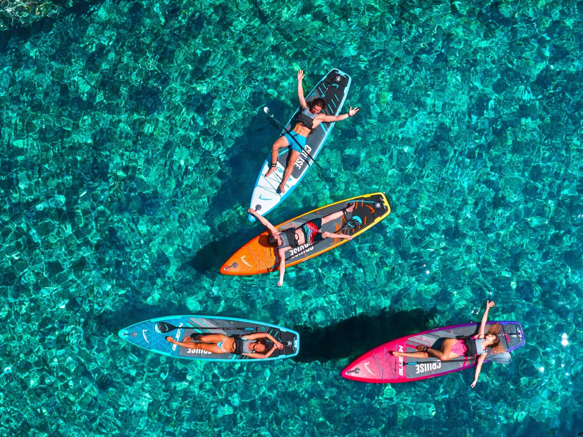 Vier Stand-Up-Paddler entspannen auf bunten Boards über klarem, türkisfarbenem Wasser